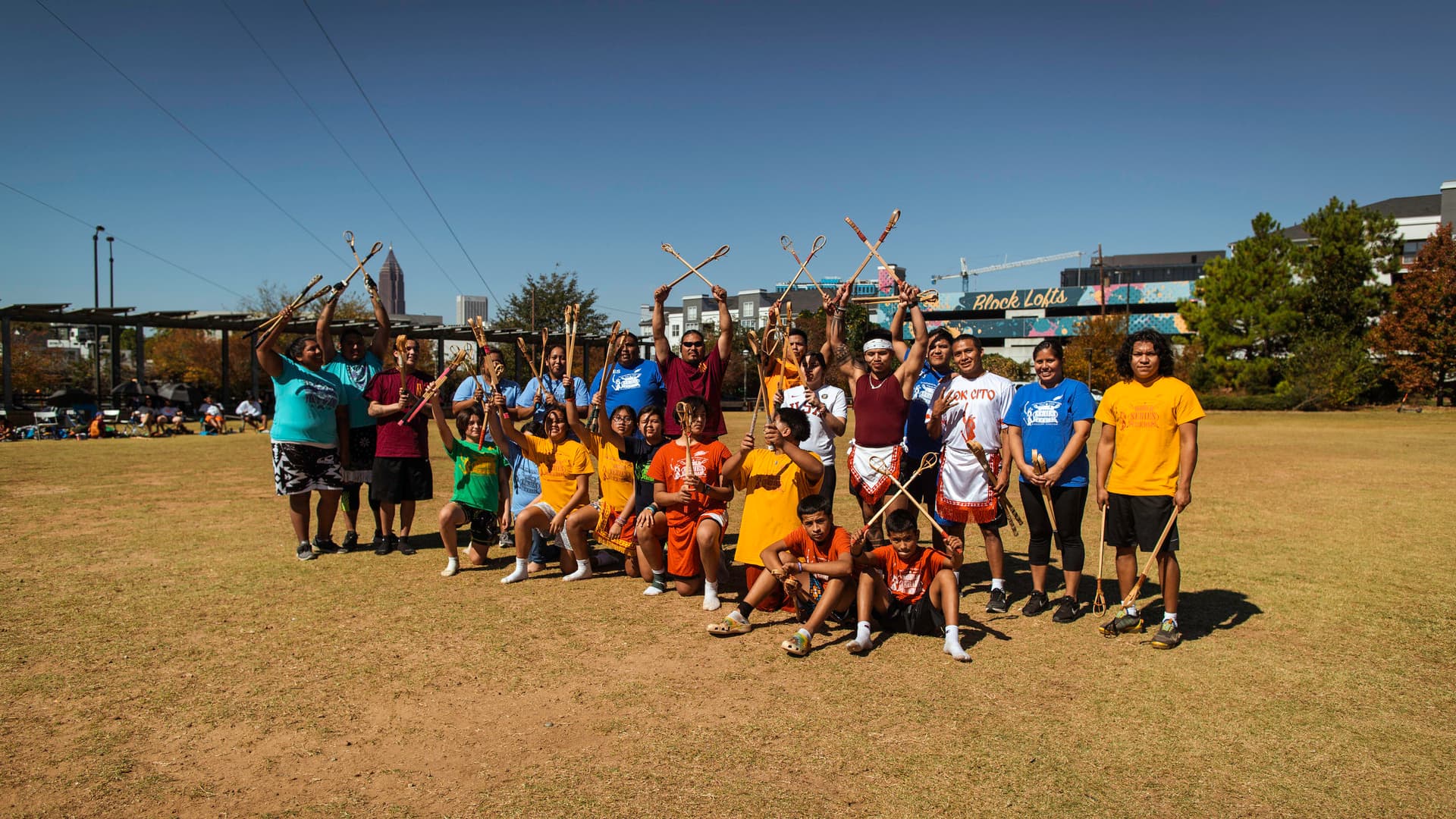 Members of Indigenous Nations pose together for a photo with their Stickball sticks on the activity field at the Historic Fourth Ward Skatepark.