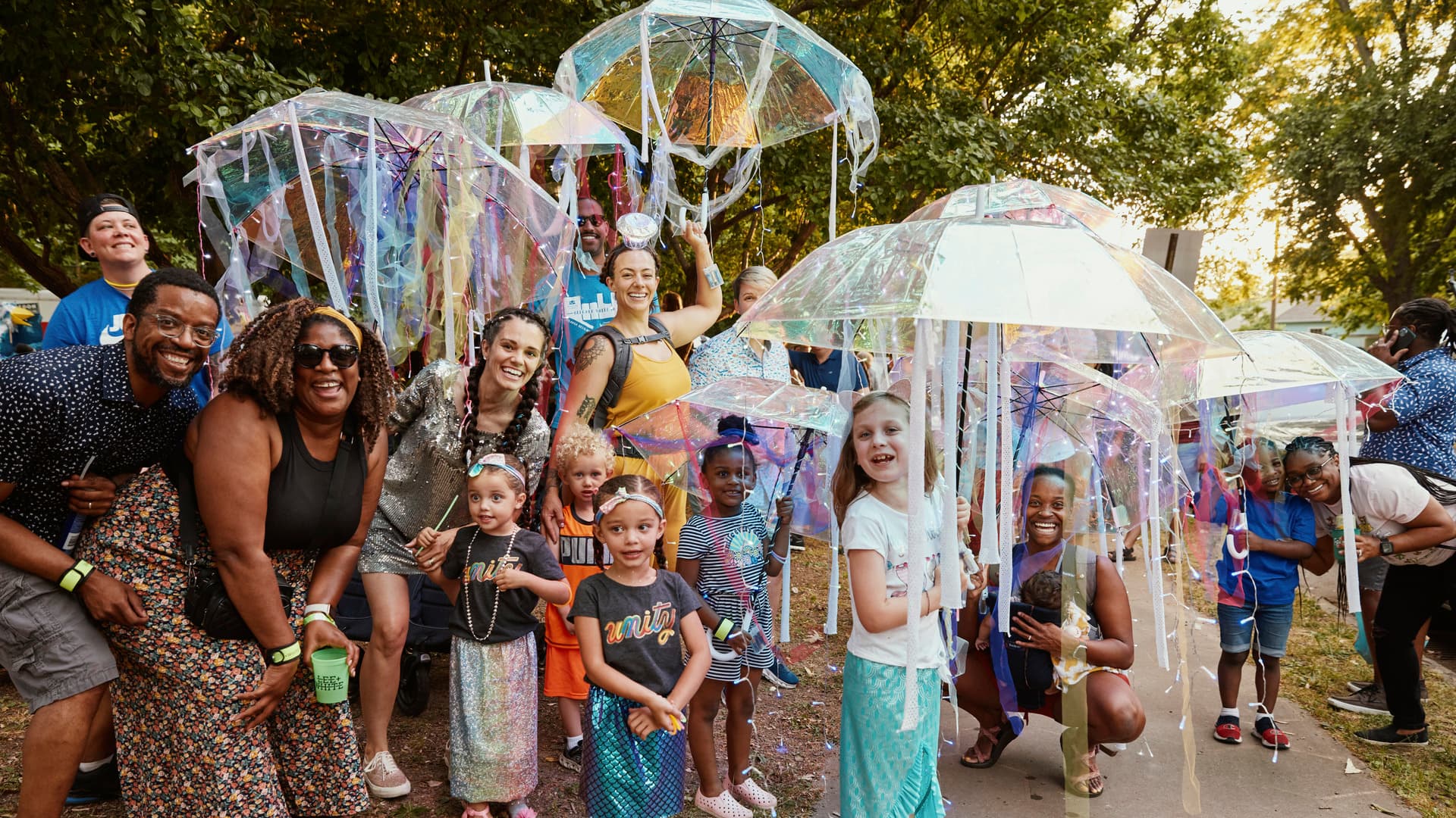 Children and their parents pose, smiling, laughing, and holding colorful parasols.