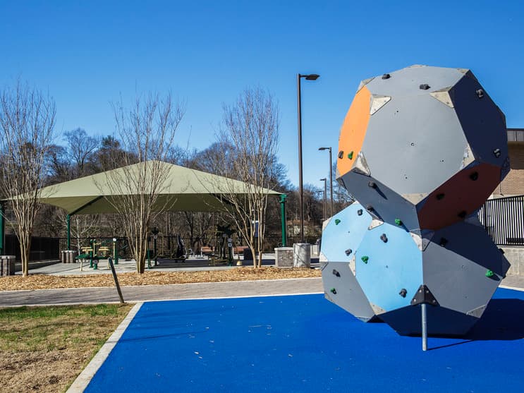 A climbing structure with bright colors stands in the foreground, while outdoor exercise equipment is visible beyond it.